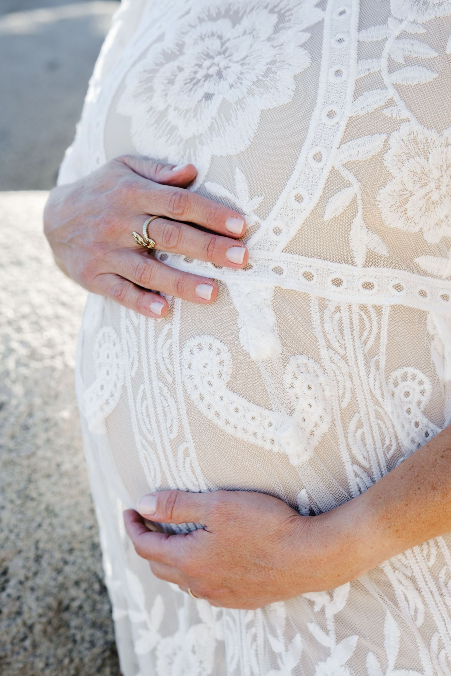 Close-up of hands touching a delicate white lace dress with floral patterns and a visible wedding ring.