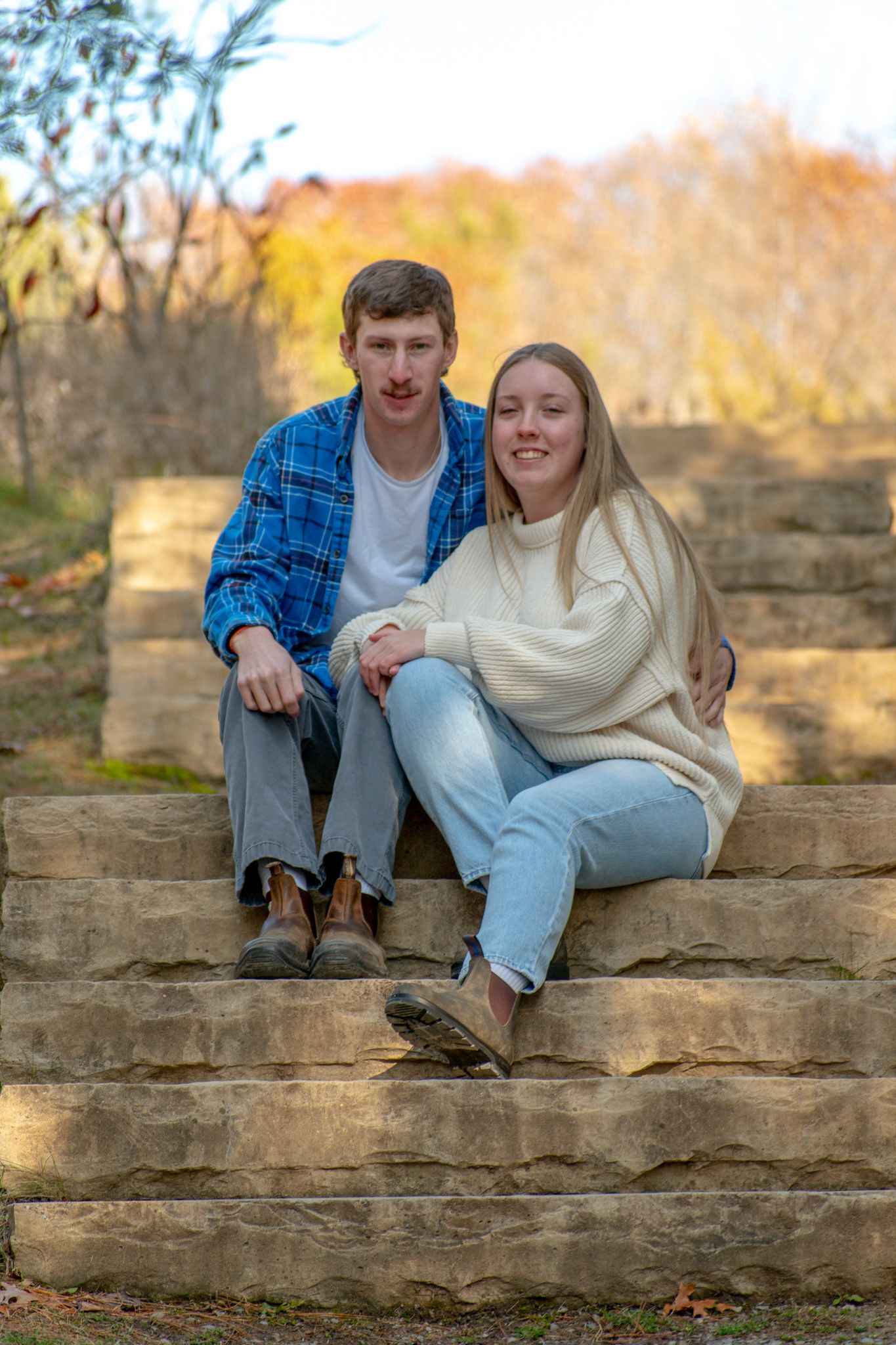 A couple shares a tender moment while sitting on stone stairs in an autumn setting.