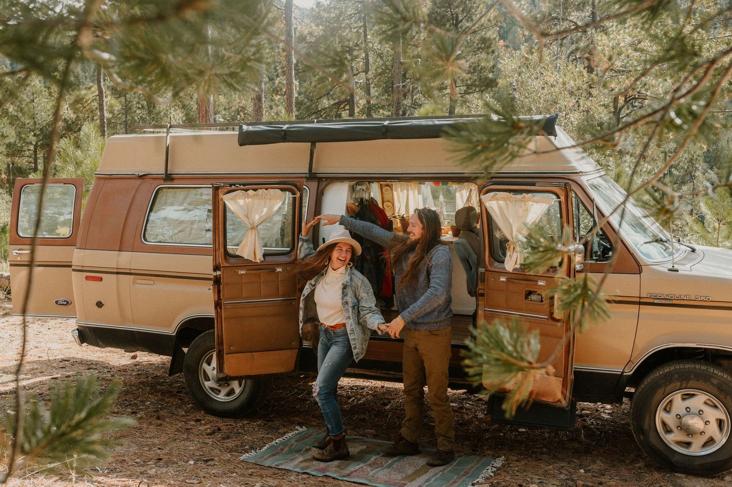 Vintage brown van parked in a wooded area with people gathered around it.