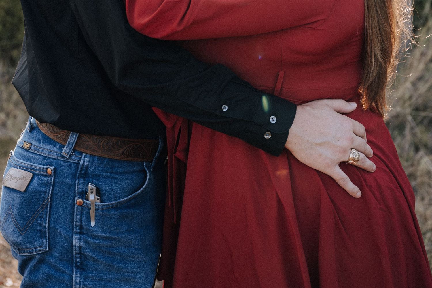 A couple embraces in casual attire with denim and a red dress shown from the waist down.