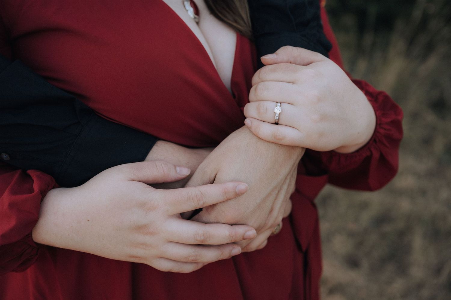Close-up shot of hands displaying an engagement ring against a red dress.