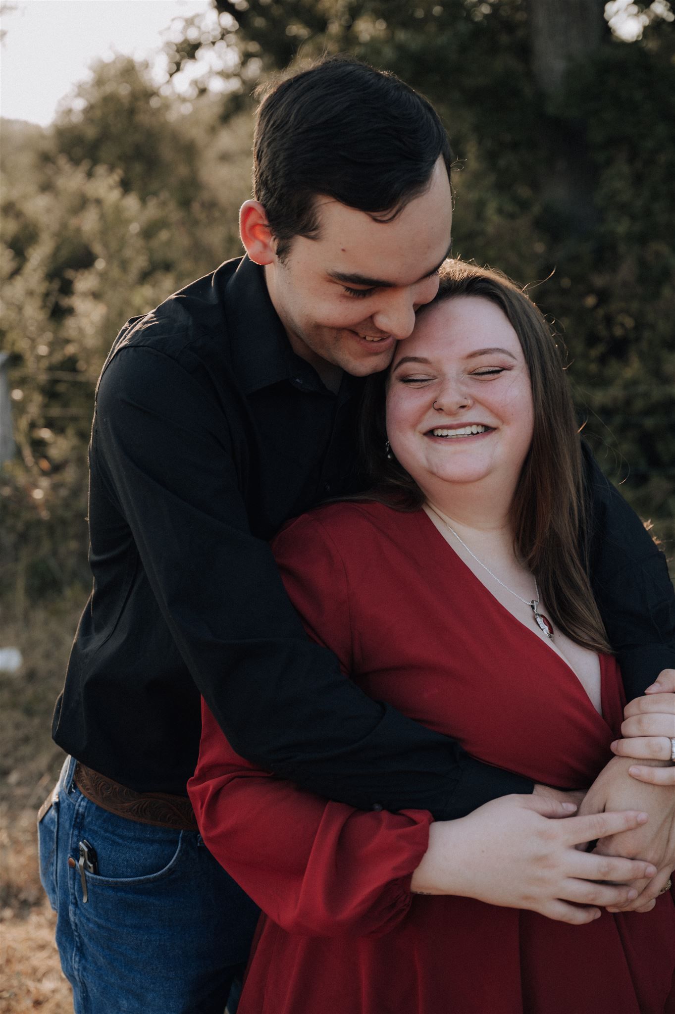 A couple shares an intimate embrace outdoors, wearing coordinated black and red outfits.