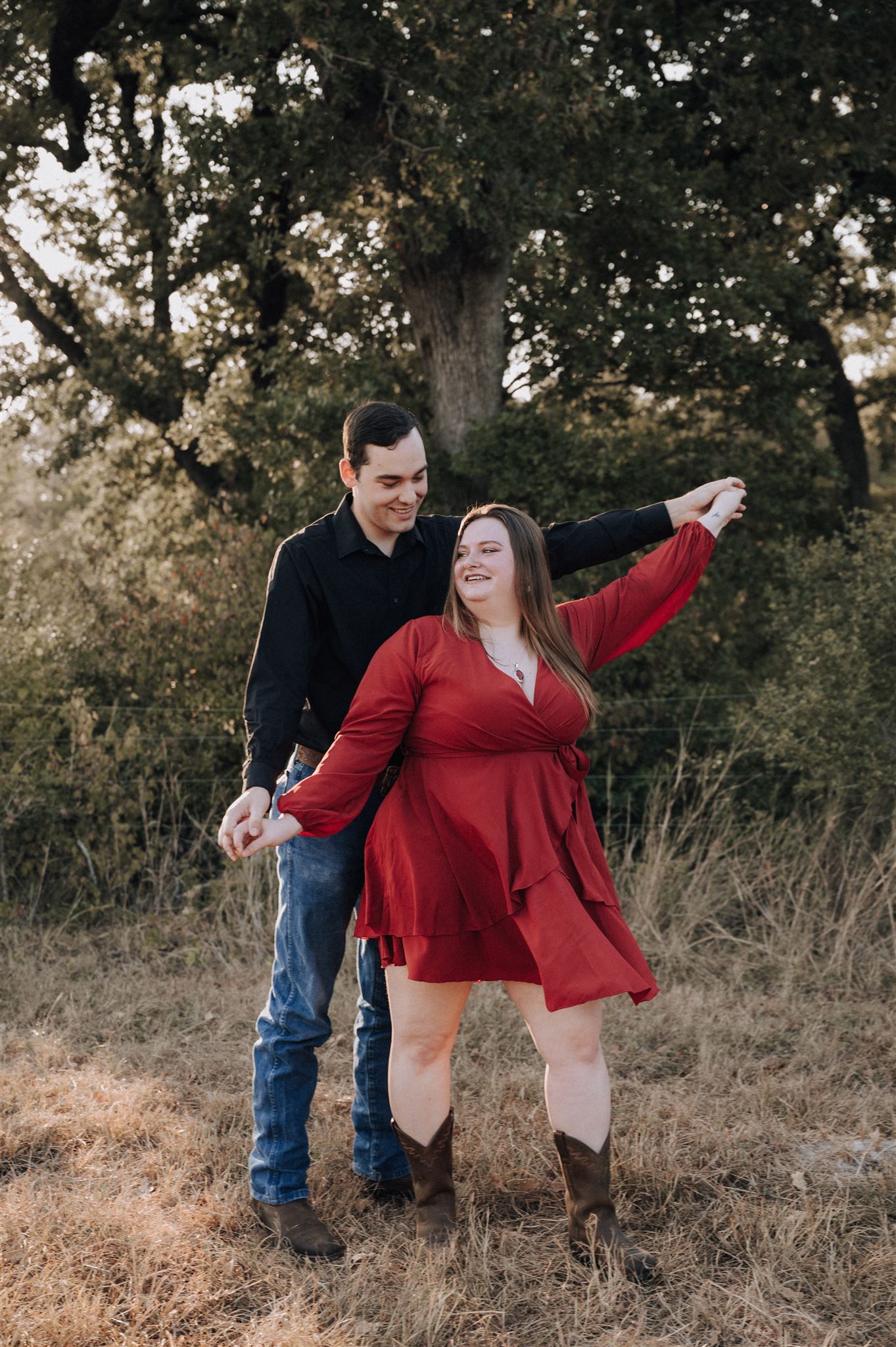 A playful couple poses in a field, with the person in red striking a joyful pose.