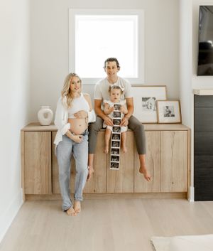 A couple in casual clothes displaying ultrasound photos on a wooden cabinet.