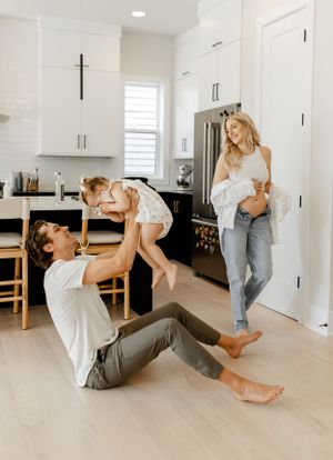 A playful family moment in a modern white kitchen with hardwood floors.