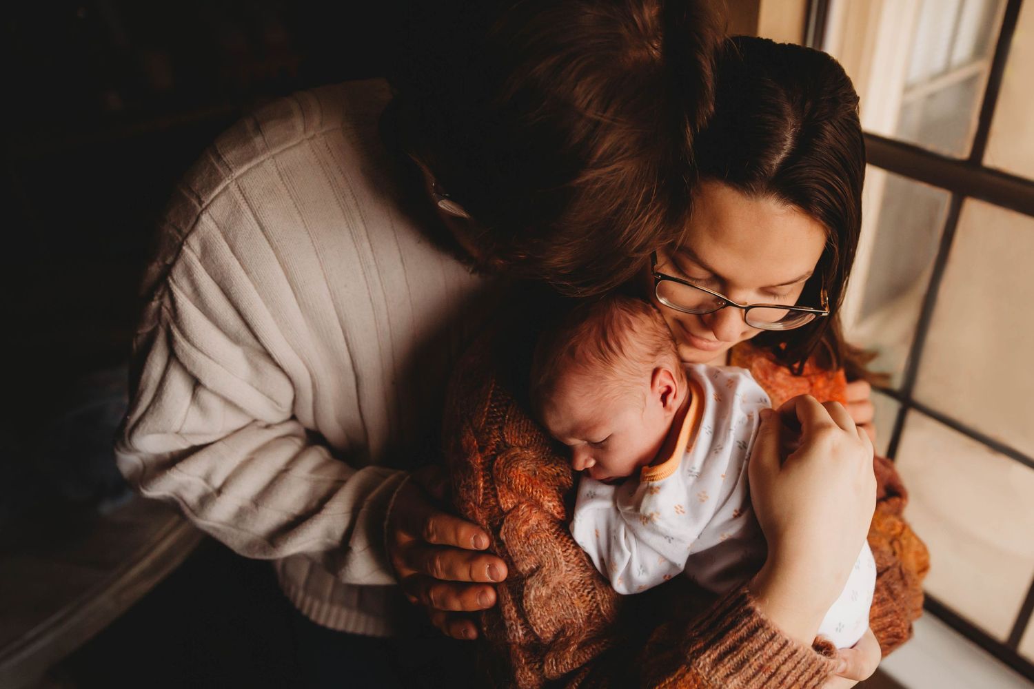 Intimate moment between parent and baby in soft natural window light.