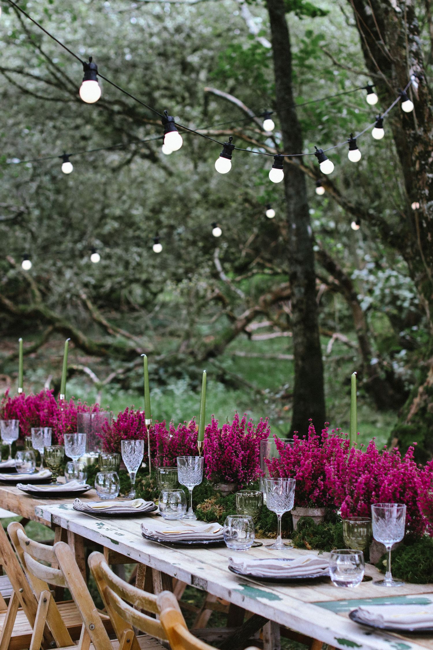 Outdoor table setting with string lights and pink flowers for elegant garden dinner party.