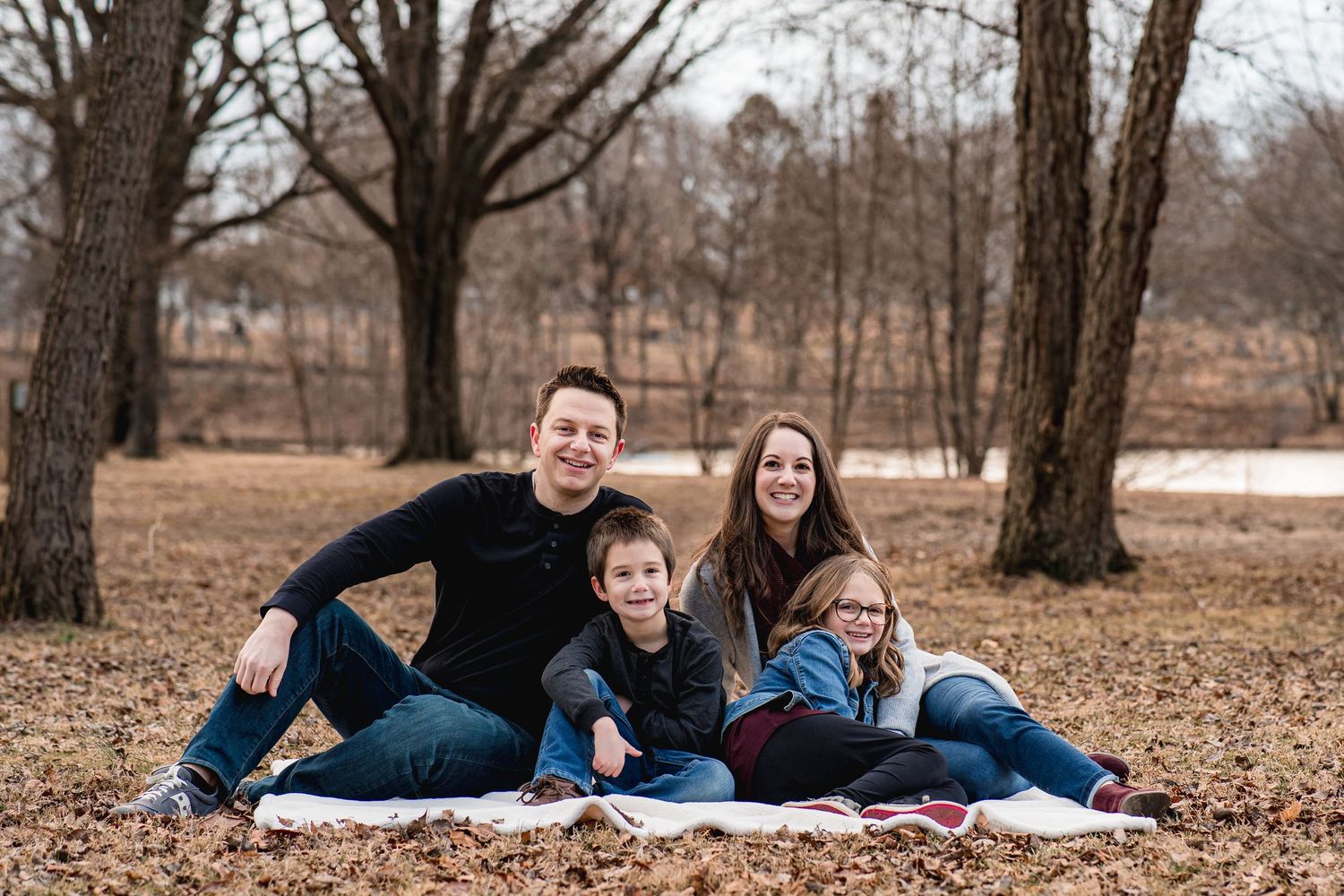 Family of four relaxing together on fallen leaves during autumn photoshoot.