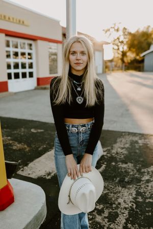 Portrait against a vintage storefront featuring casual western style with jeans and a white hat.