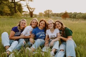Group wearing casual denim sitting together in sunny grass field at sunset.