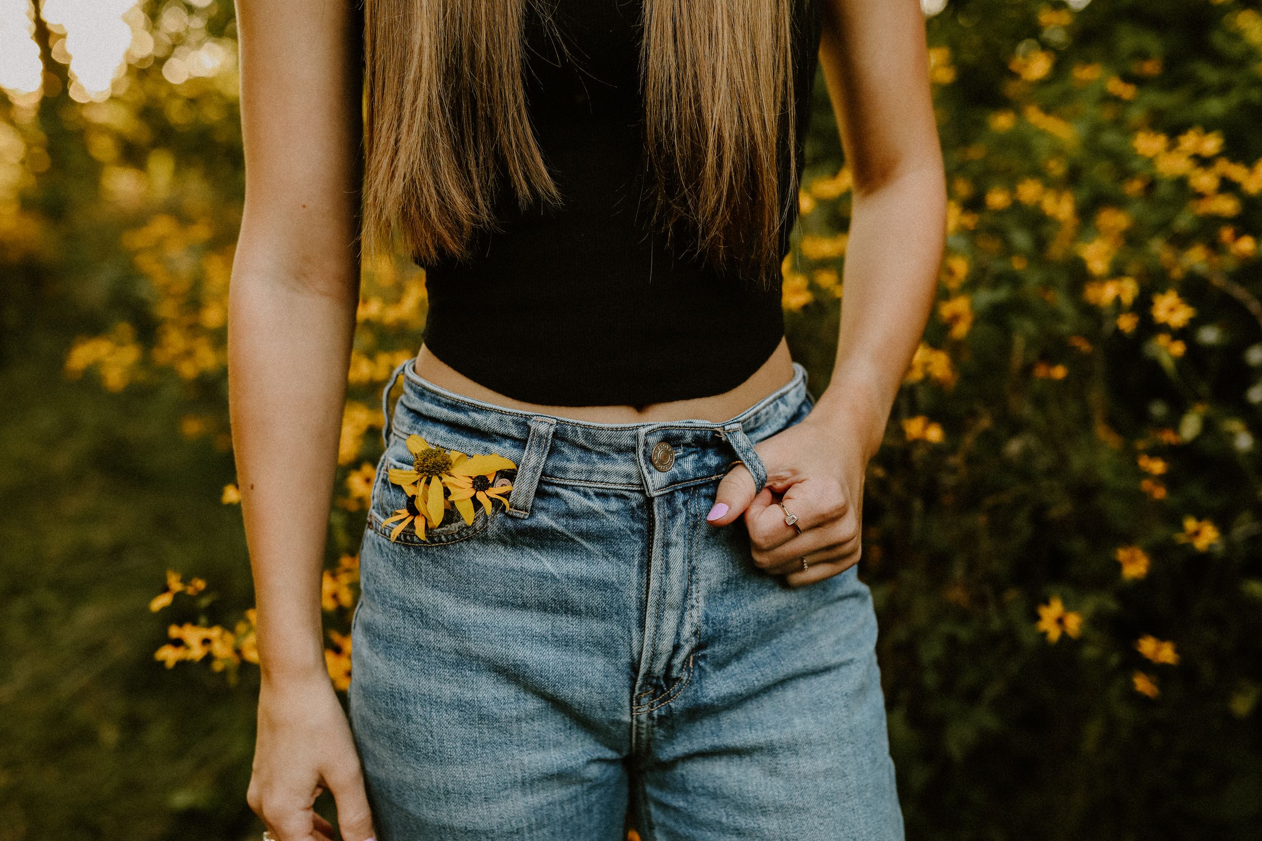 Sunflowers tucked into the pocket of light wash denim jeans against a golden sunset background.