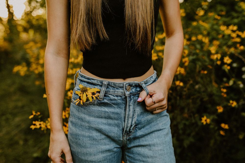 Sunflowers tucked into the pocket of light wash denim jeans against a golden sunset background.