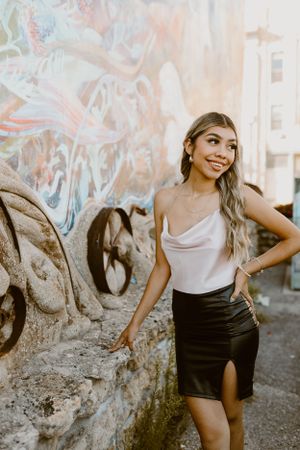 Person in elegant outfit poses against colorful graffiti wall background.
