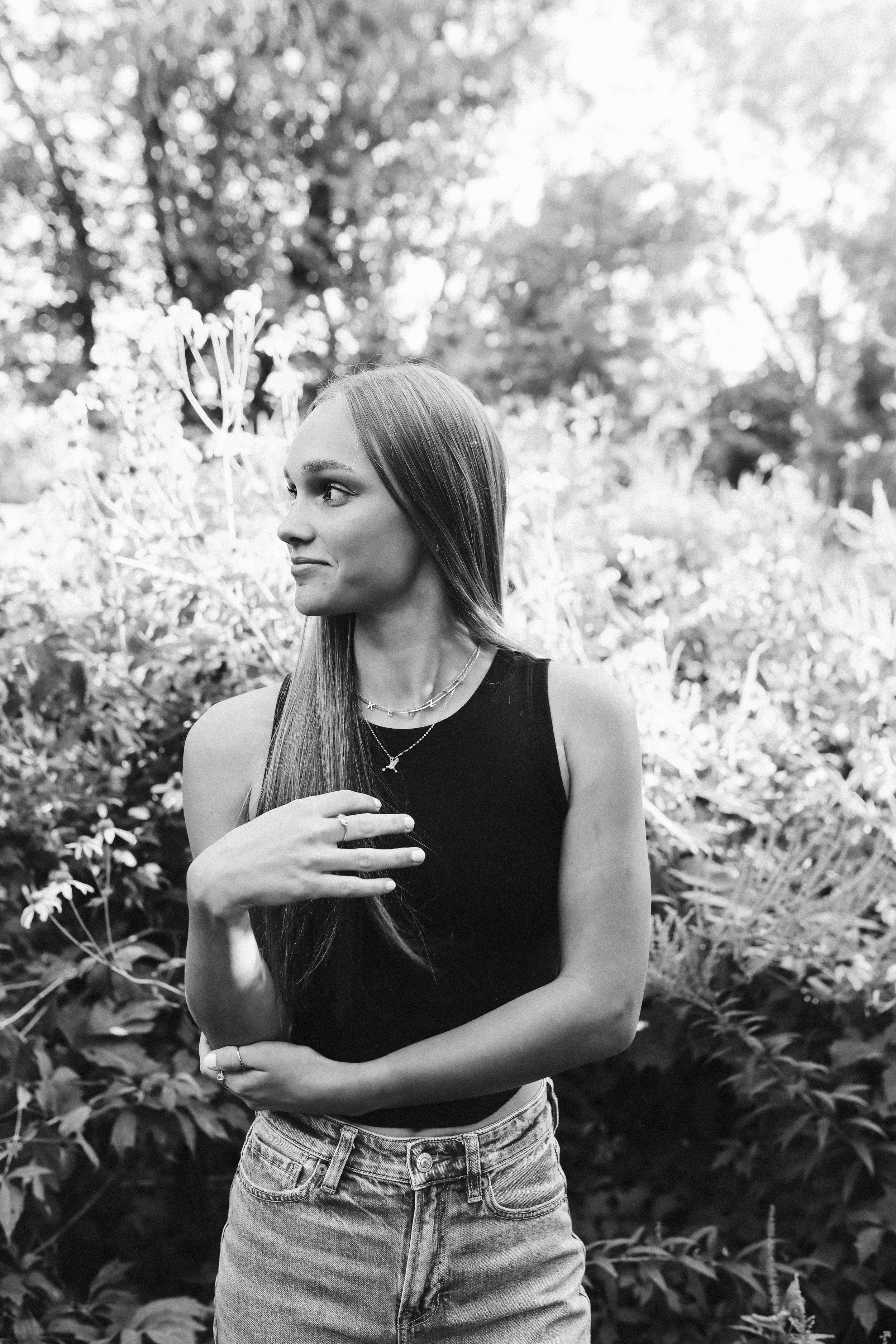 Black and white portrait of someone in casual attire against natural foliage.