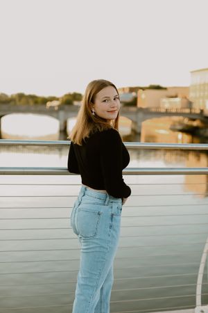 Sunset portrait on a riverside boardwalk with urban architecture in the background.