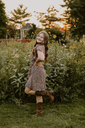 Person wearing floral dress poses playfully in garden during golden hour.