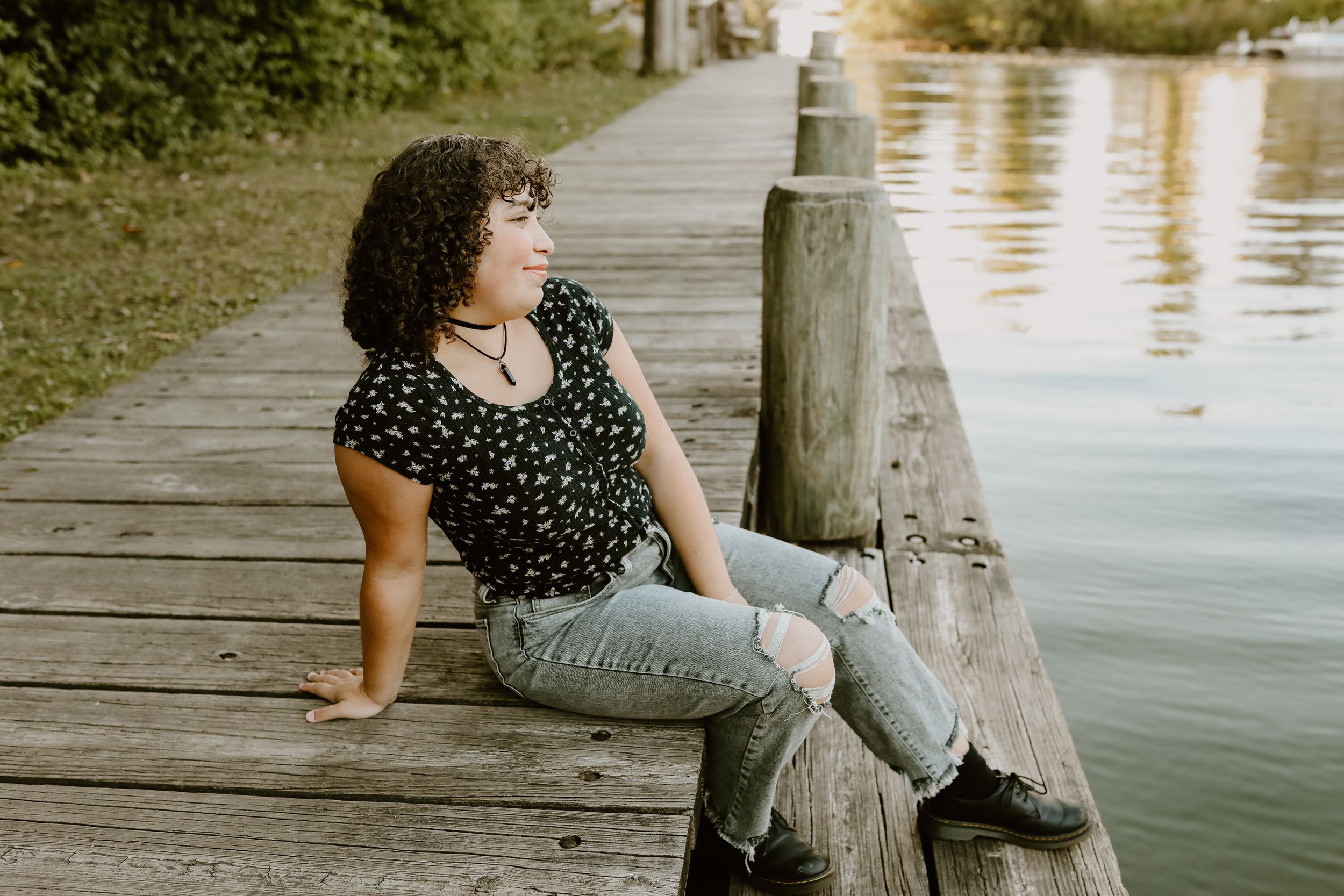Person sitting casually on wooden dock by calm water.
