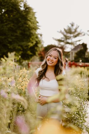 Person posing in a sunny garden filled with wildflowers and greenery.