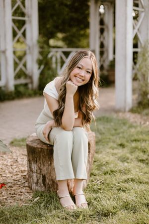 Person sitting and smiling on a wooden log in a rustic outdoor setting.