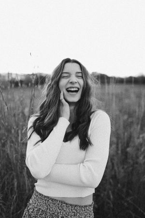 Candid black and white portrait of someone laughing joyfully in a field wearing a white sweater.