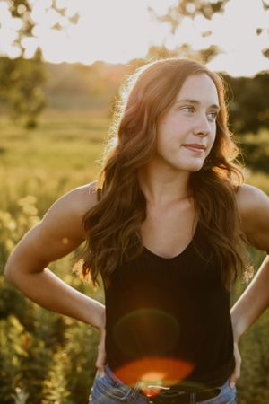 A woman poses in a black tank top during golden hour in a summer field.