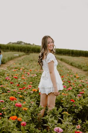 Person in white dress standing in a vibrant flower field with orange and pink blooms.