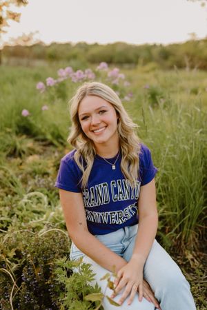 Student in Grand Canyon University shirt poses outdoors among wildflowers during golden hour.