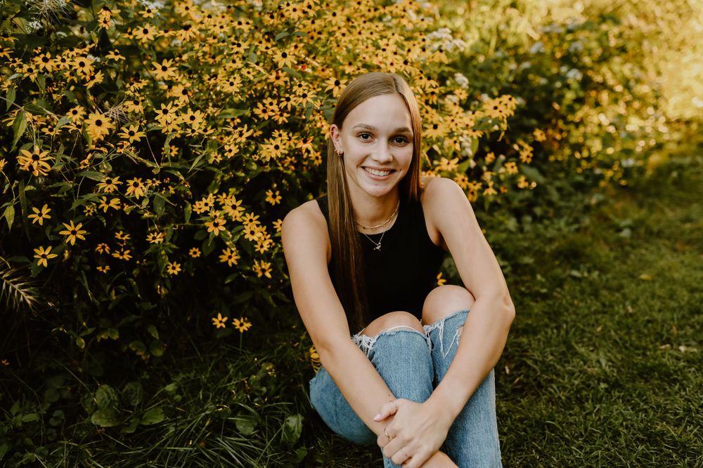 Person sitting on grass near blooming yellow flowers in casual attire during golden hour.