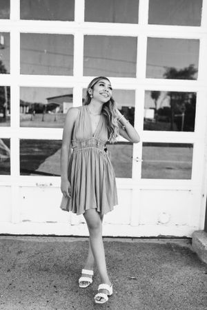 Person in flowing dress poses joyfully against white geometric window background.