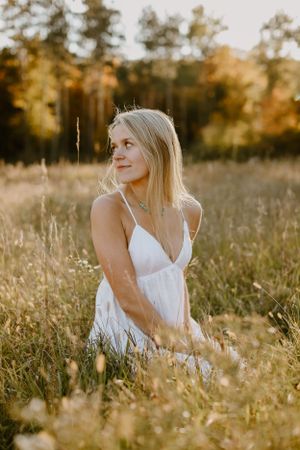 A portrait in a golden field at sunset shows someone in a flowing white dress among tall grass.