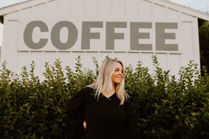Person in black standing by a white building with large COFFEE text signage.