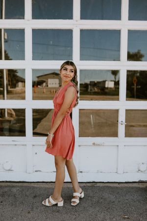 Person in coral dress poses against white geometric window pattern background.