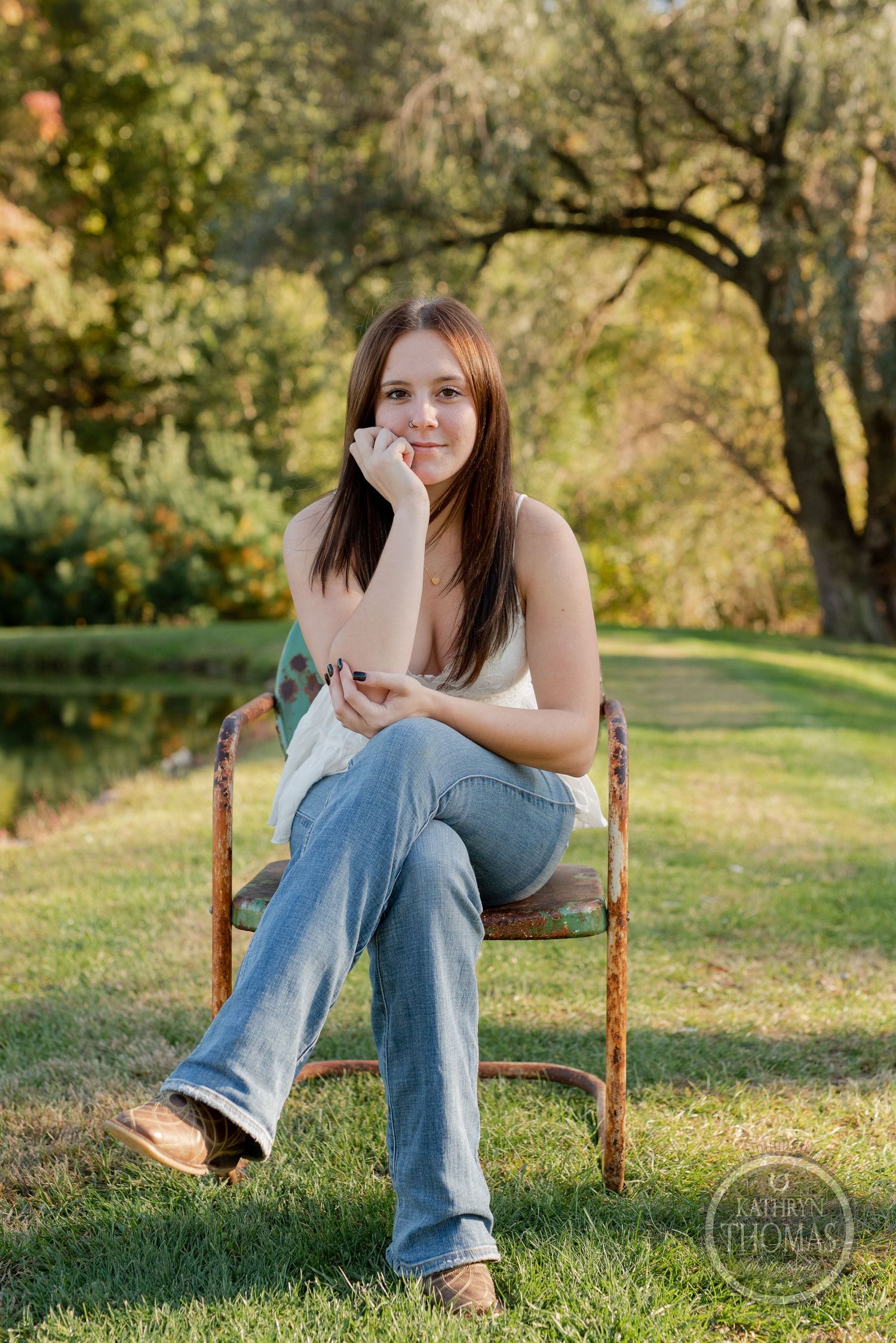 Casual portrait on rustic chair with scenic fall foliage and pond backdrop.