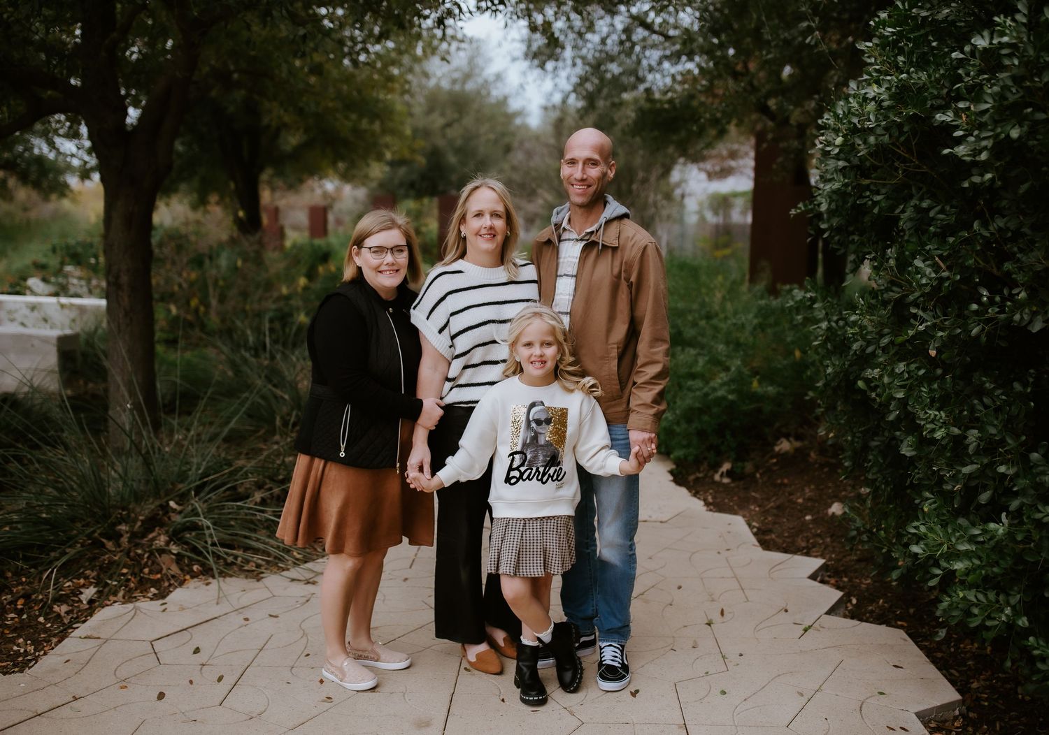 A casual family of four poses together on a garden pathway during an autumn day.
