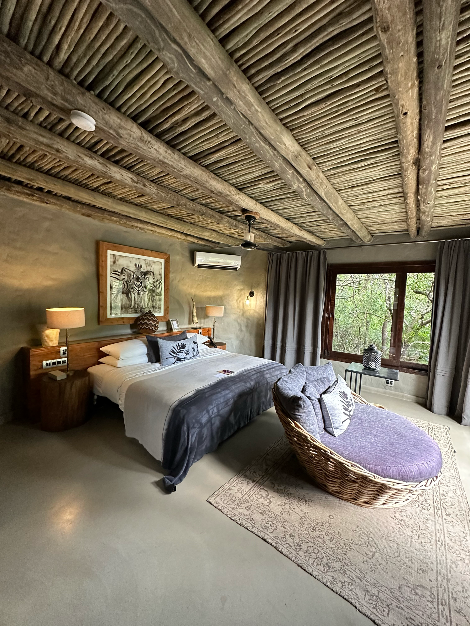 Luxurious bedroom suite with rustic thatched ceiling and panoramic nature views.