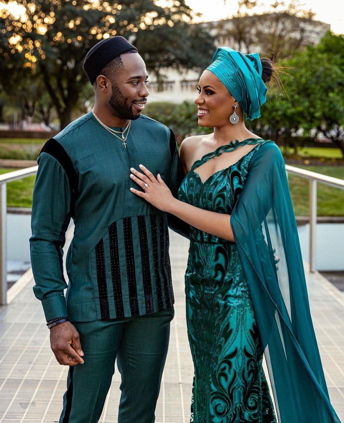 Couple in coordinated teal outfits smiling at each other outdoors.