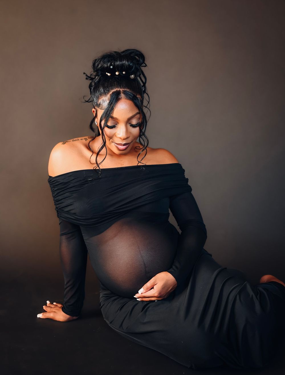 Pregnant woman in elegant black off-shoulder gown poses gracefully during a professional maternity photoshoot.