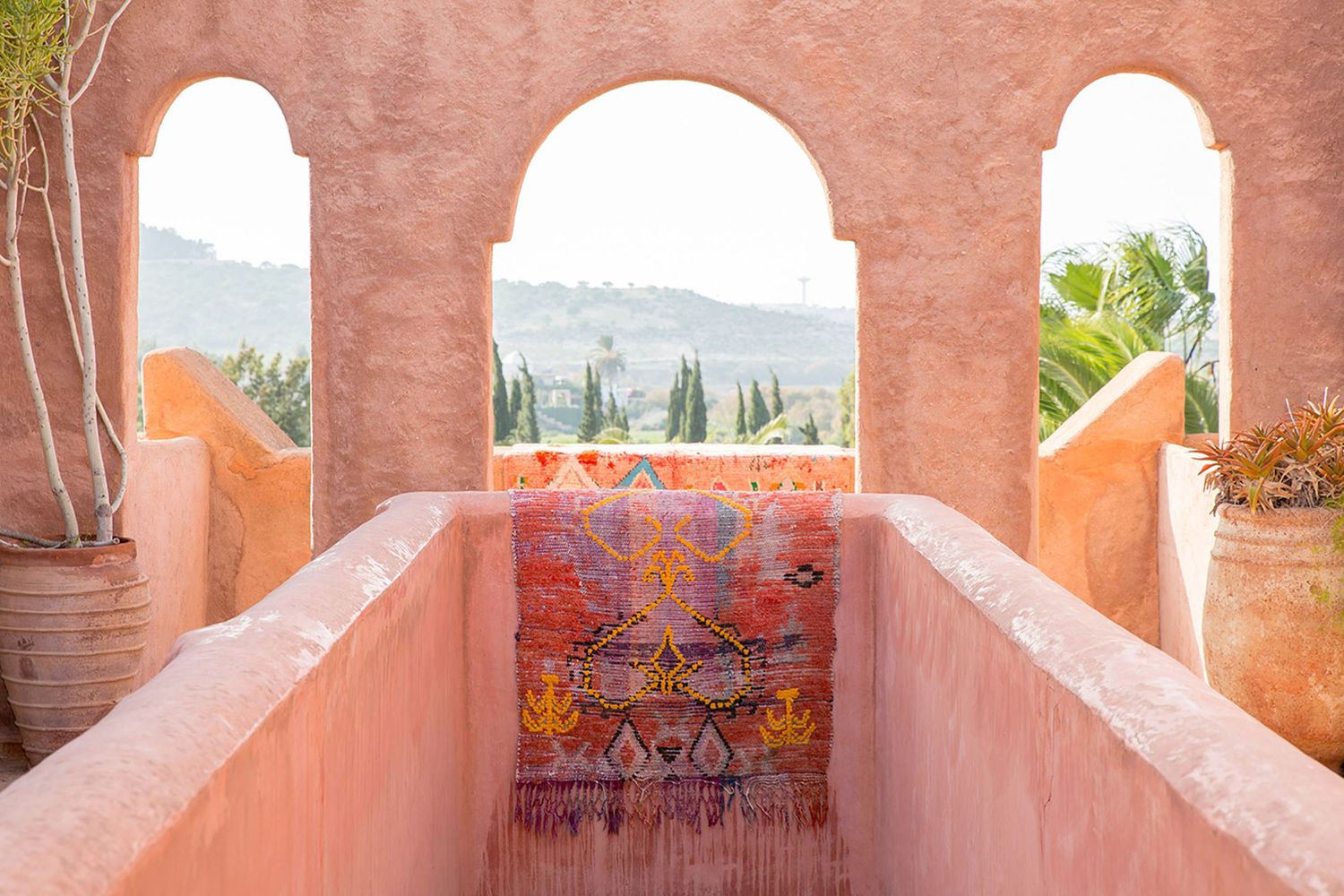 Mediterranean-style terrace with pink walls and arched doorways overlooking mountains.
