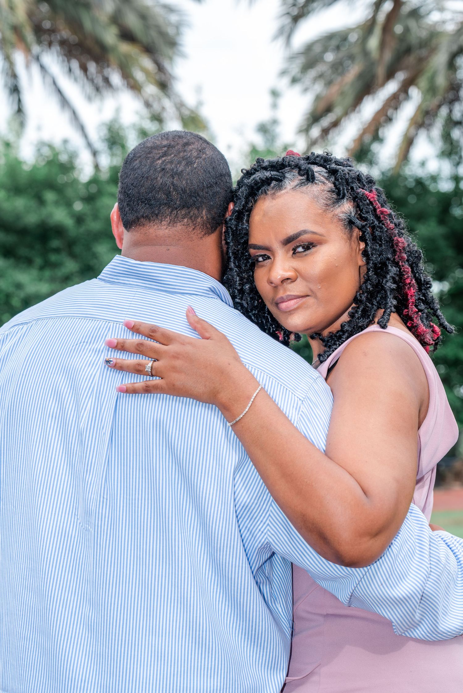 Intimate couple wearing pink and blue striped shirts embracing outdoors in a romantic photoshoot series.