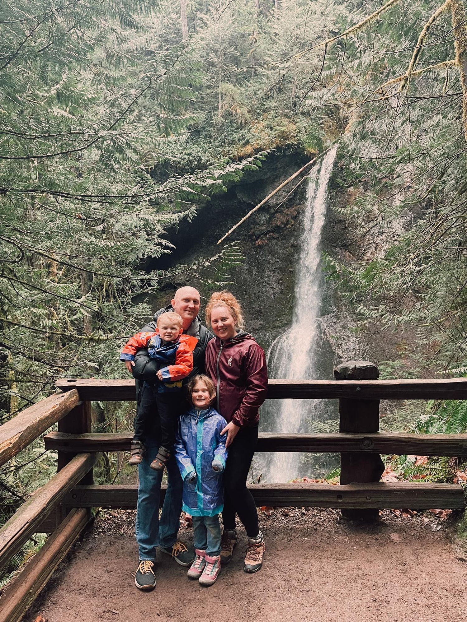 Group poses together on wooden viewing platform with waterfall cascading in misty forest background.