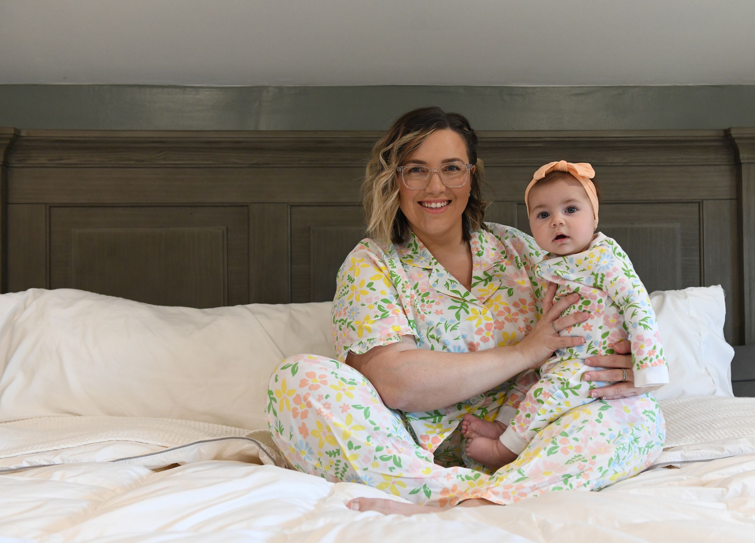 A parent and baby wearing matching floral pajamas cuddle together on a bed.