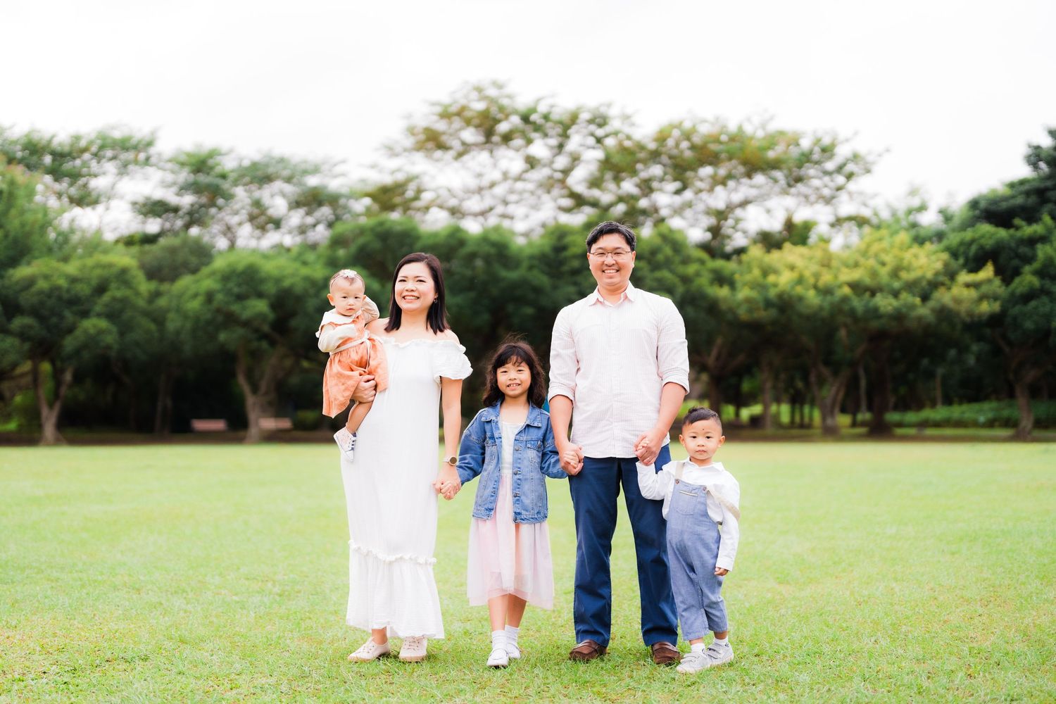 Family poses together on green lawn with trees in background.