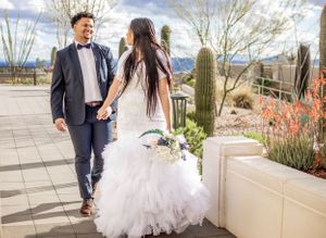 Elegant Tucson wedding portrait of a bride and groom walking together surrounded by Arizona desert plants and mountains.