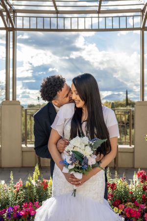 Romantic Tucson wedding photo of newlyweds kissing under a modern pergola with desert scenery and colorful florals.