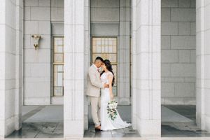 Tucson wedding photographer capturing a bride and groom posing beneath tall white stone pillars in elegant architecture.