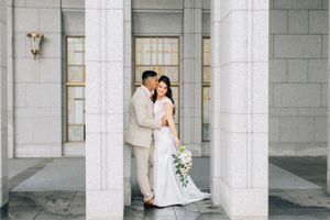 Tucson wedding photography of a bride and groom embracing between tall stone columns at a temple-style venue.
