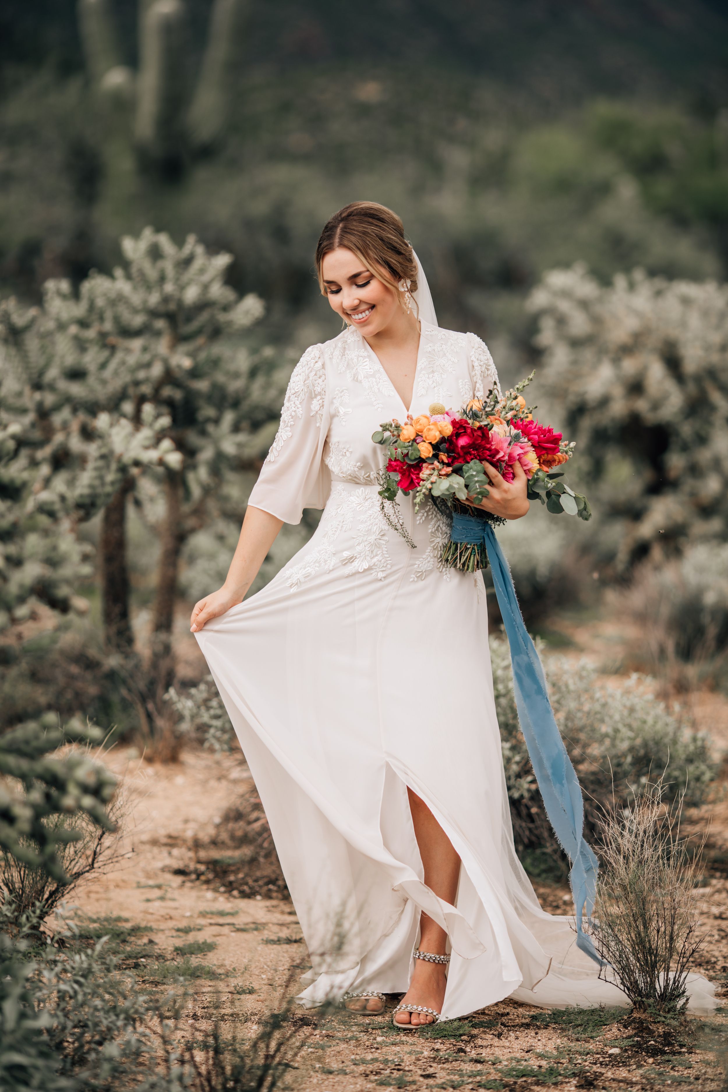 Tucson bridal portrait of a bride walking through the desert holding a colorful bouquet with soft golden light.