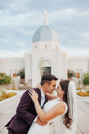 Tucson wedding photo of a bride and groom kissing in front of a white temple with a dome and desert landscaping.