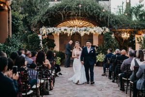 Tucson wedding ceremony photo of a bride walking down the aisle with her father at an outdoor venue surrounded by guests.
