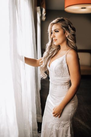 Tucson bridal photo of a bride standing by a window curtain with soft natural light highlighting her dress.